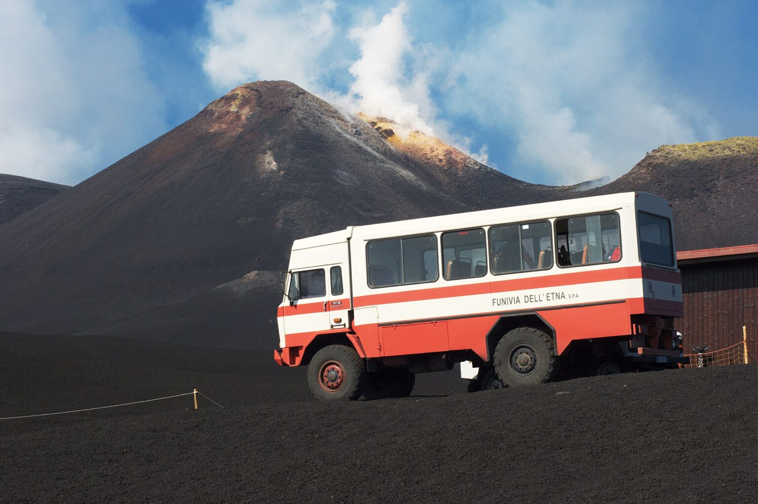 Bus fuoristrada 4x4 della funivia dell'Etna con un cratere fumante sullo sfondo