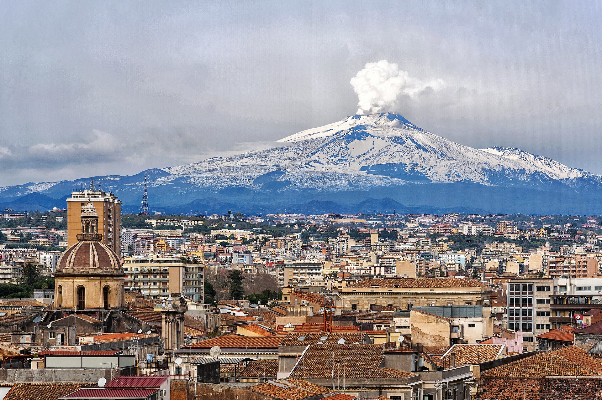 Skyline di Catania con l'Etna innevata e pennacchio attivo sullo sfondo