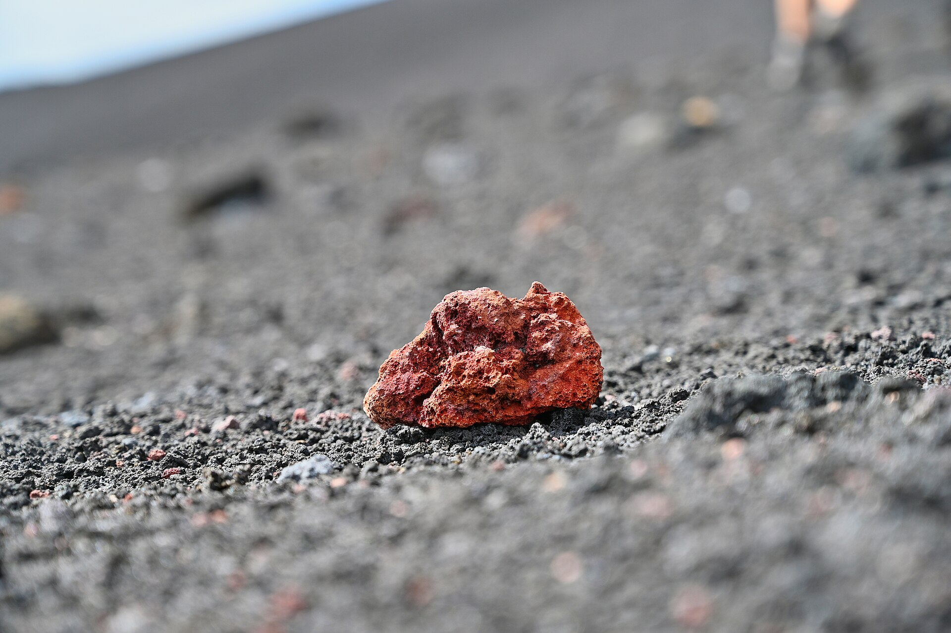 Frammento di roccia lavica rossastra sul terreno di cenere vulcanica dell'Etna